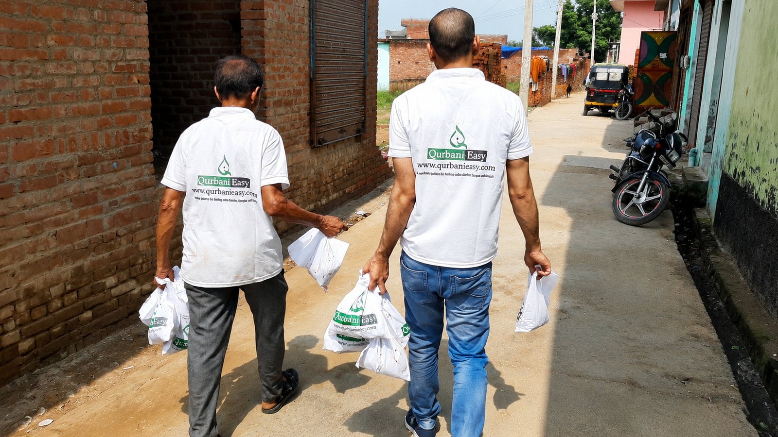 Qurbani Easy volunteers carrying meat distribution bags down a village lane